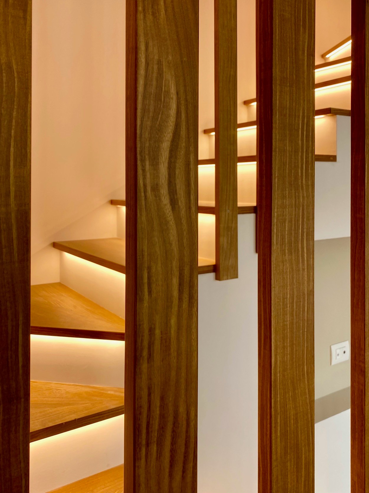 Tra le doghe di rovere del parapetto, una scala di legno con una sottile linea di luce sotto ogni gradino